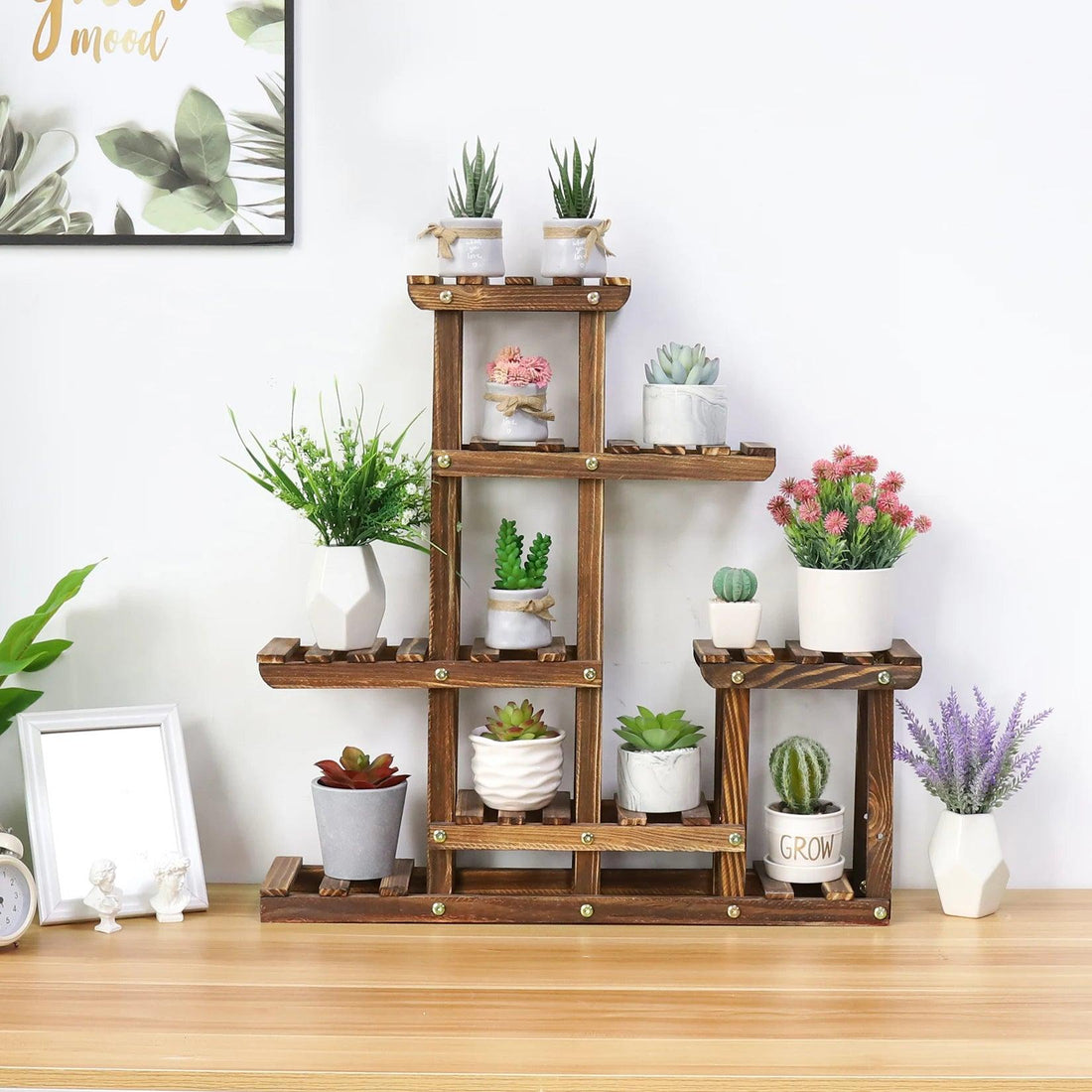 A 6-tier wooden plant stand made of pine wood, displaying various potted plants, placed on a wooden table against a white wall.
