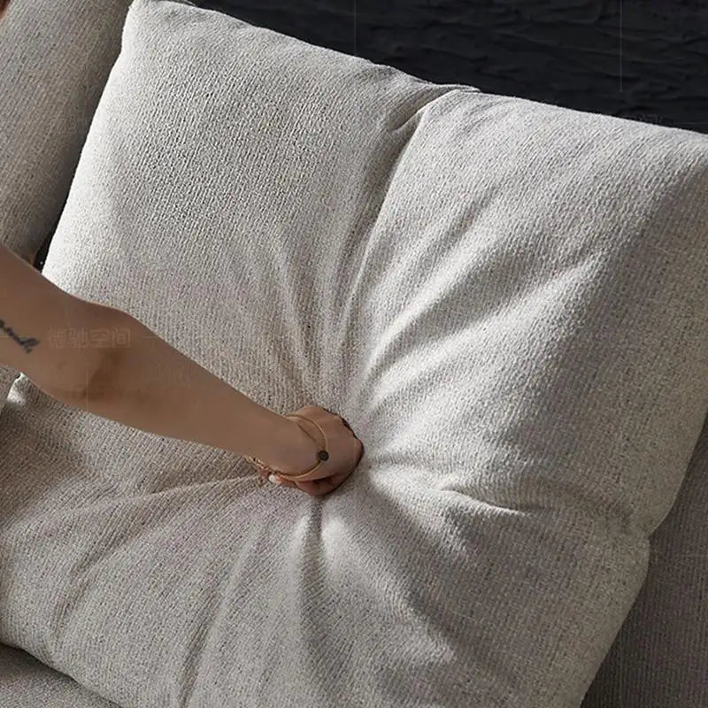 Person adjusting a light gray pillow on a sofa