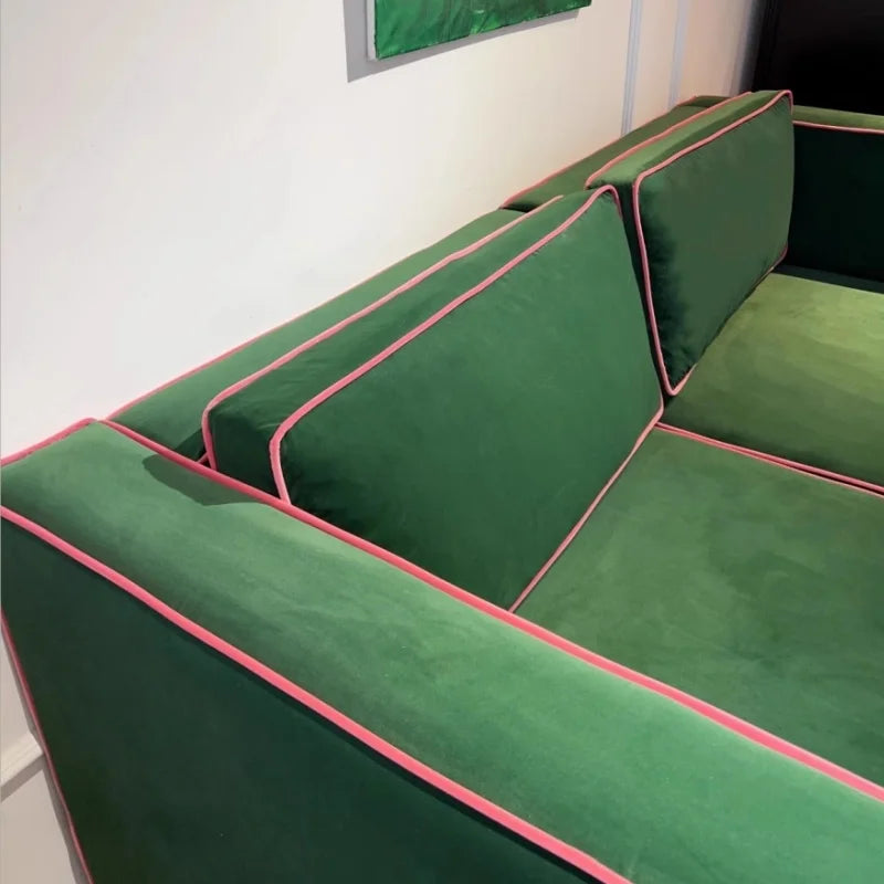 Green corner sofa with pink piping against a white wall.