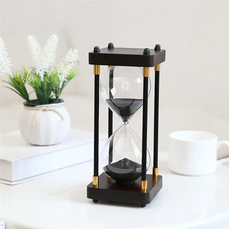 Black and gold hourglass on a white surface with a plant and books in the background