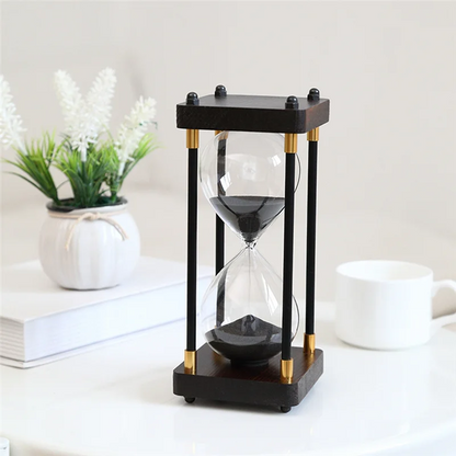 Black and gold hourglass on a white surface with a plant and books in the background