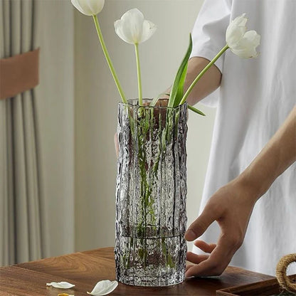 Clear glass vase with white tulips on a wooden table, person in white shirt partially visible