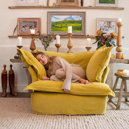 Woman lying on a yellow armchair in a cozy living room with candles and framed pictures.