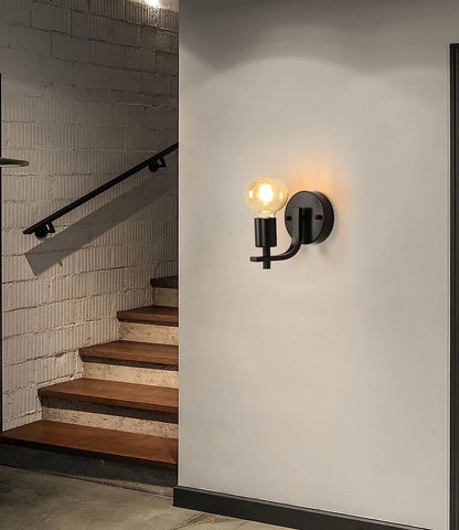 Wall-mounted light fixture on a white wall next to a staircase with brick walls.