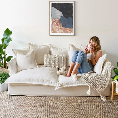 Woman sitting on a beige sofa in a cozy living room, holding a mug.