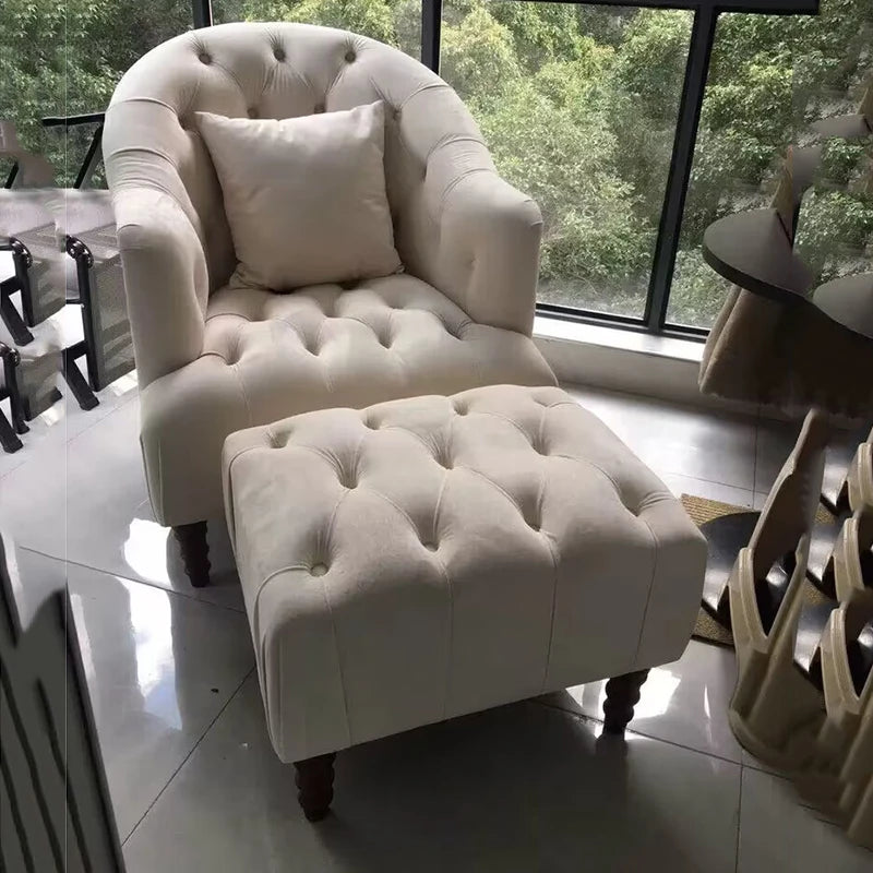 White tufted armchair with matching ottoman in a room with large windows.
