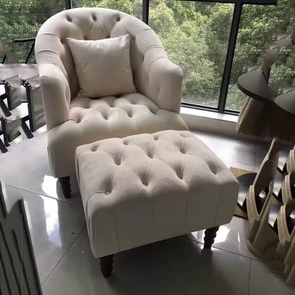 White tufted armchair with matching ottoman in a room with large windows.