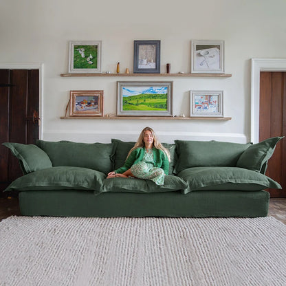 Woman sitting on a green sofa in a living room with framed pictures on the wall.