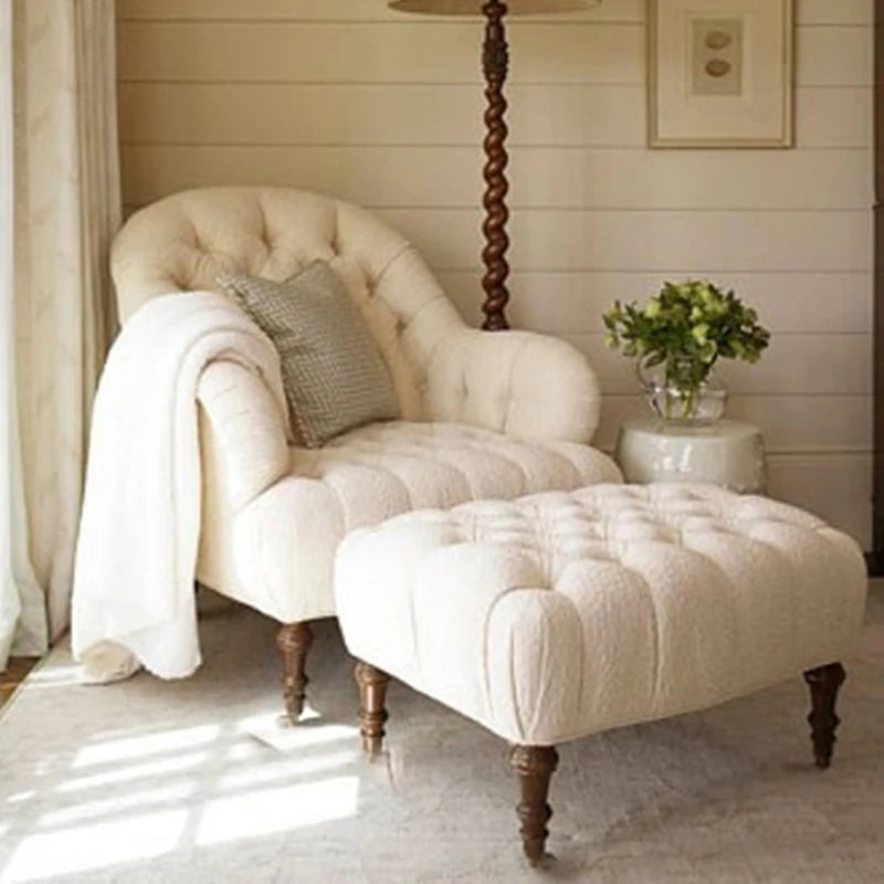 White upholstered armchair with matching ottoman in a room with wooden floor and lamp.