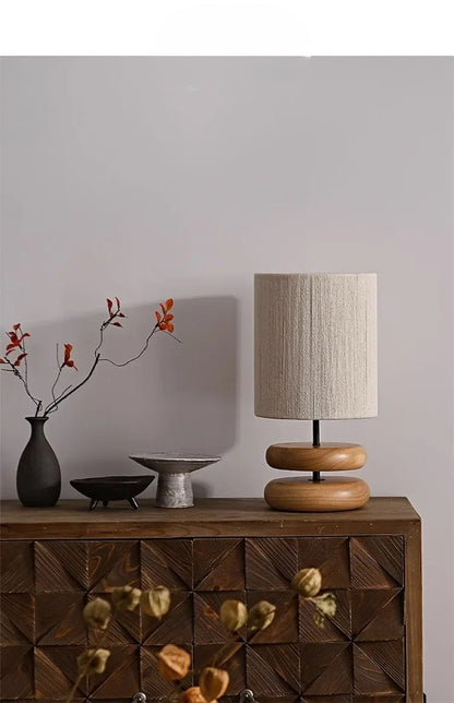 Wooden sideboard with a lamp, vase, and decorative items against a plain wall.