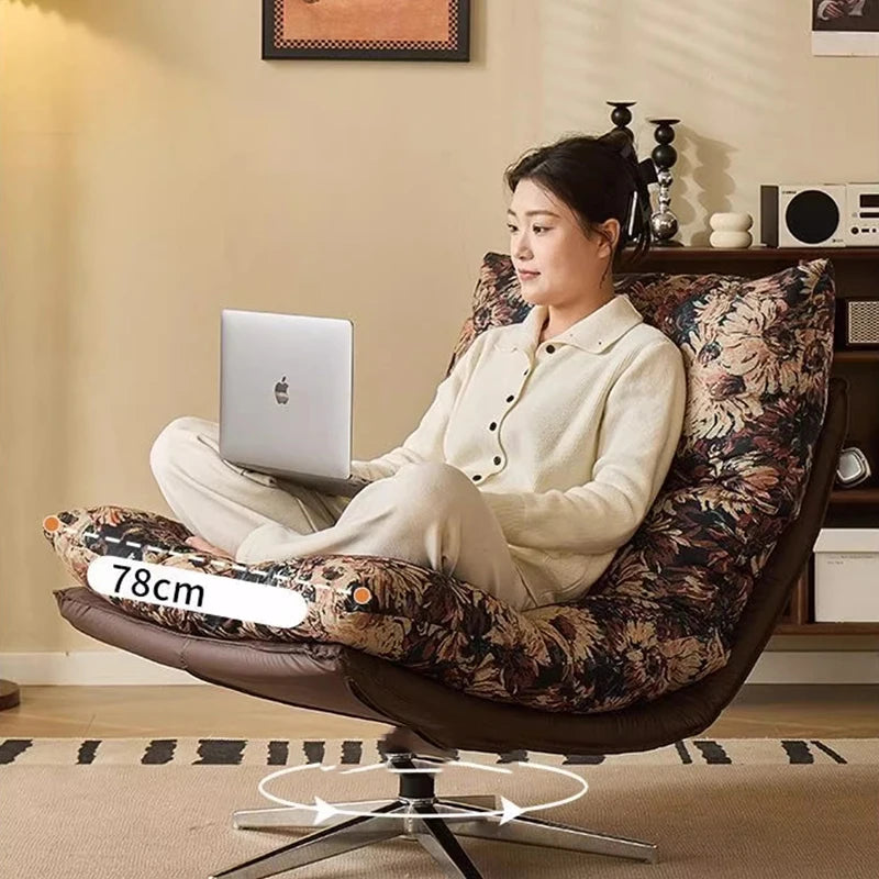 Woman sitting on a floral-patterned chair using a laptop in a cozy room.