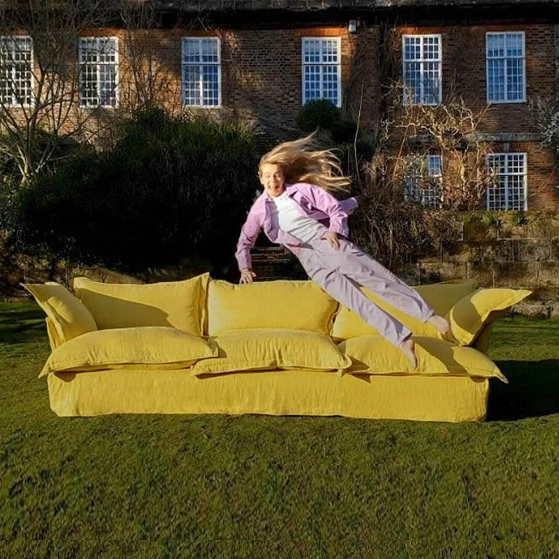 Person sliding down a large yellow sofa in a garden with a brick building in the background