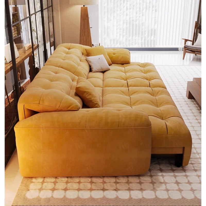 Yellow sectional sofa in a living room setting with a rug and bookshelf.