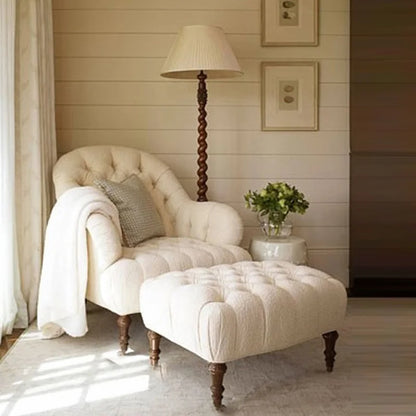 Cozy living room with a cream-colored armchair and ottoman, lamp, and framed pictures.
