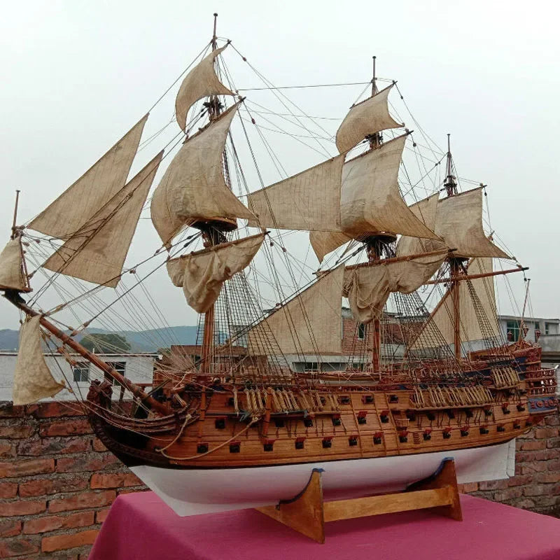 Model of a three-masted sailing ship on a pink surface with a brick wall background