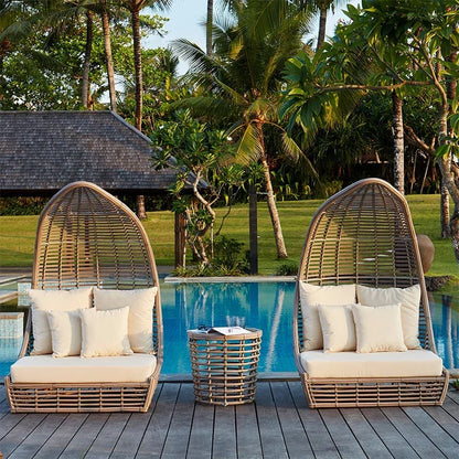 Person enjoying a drink and relaxing on an outdoor rattan sun lounger.