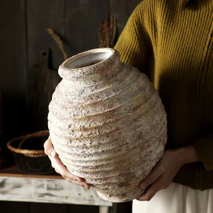 Person holding a textured ceramic vase in a warm indoor setting