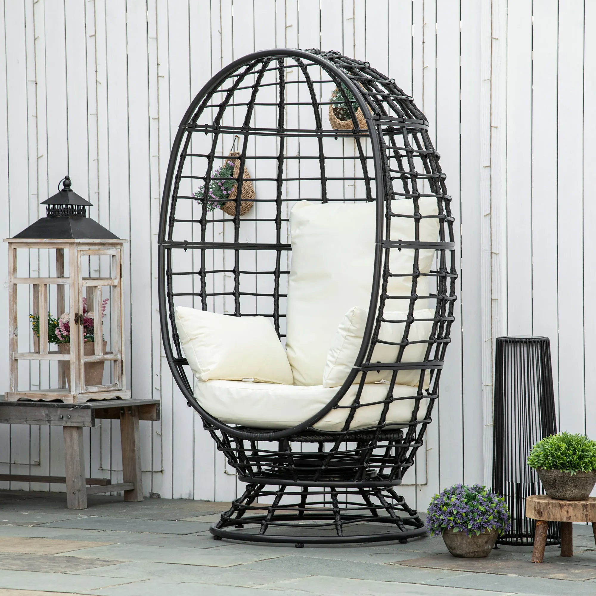 Black wicker egg-shaped chair with white cushions in an outdoor setting.