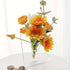 Clear glass vase with orange and yellow flowers on a white surface