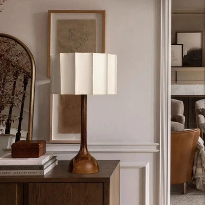 Table lamp with wooden base and white shade on a side table in a room setting.