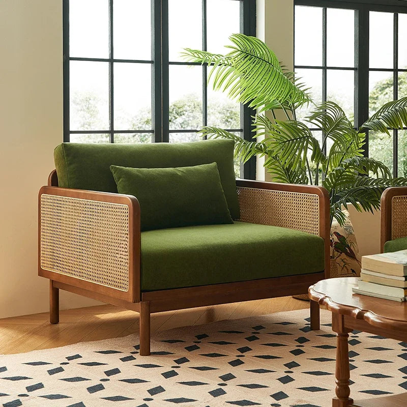 Green sofa with wicker backrest in a room with large windows and plants.