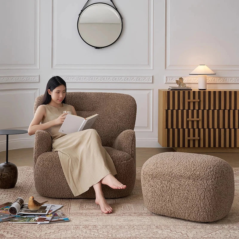 Woman reading a book in a brown armchair with a matching ottoman in a stylish room.