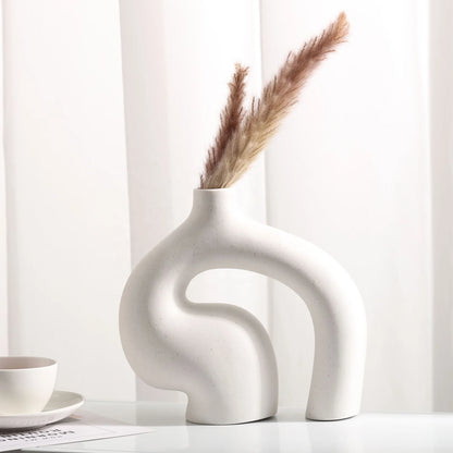White abstract vase with dried pampas grass on a white surface with a white curtain background