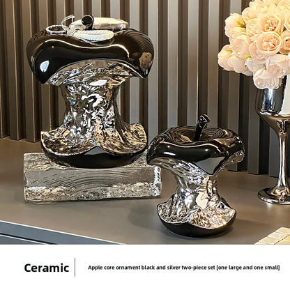 Ceramic apple core ornaments in black and silver on a surface with a striped wall in the background.