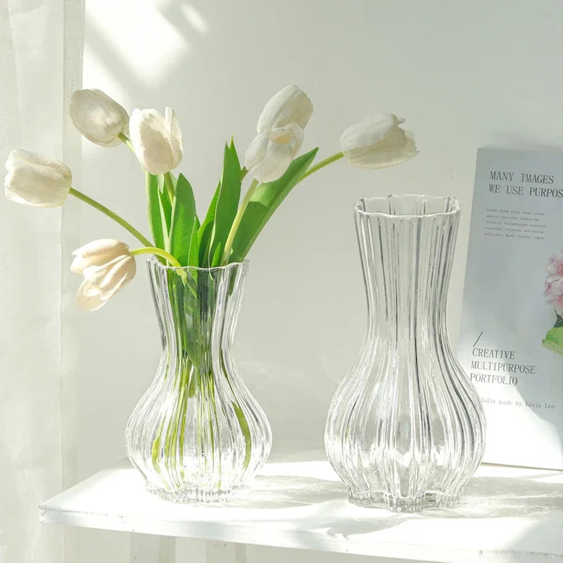 Two clear glass vases with white tulips on a white surface.