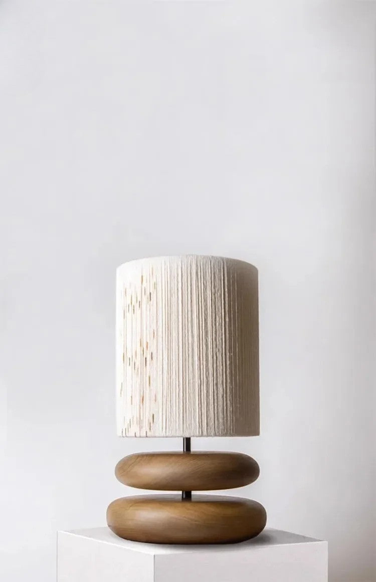 Table lamp with wooden base and textured white shade on a white pedestal against a light gray background