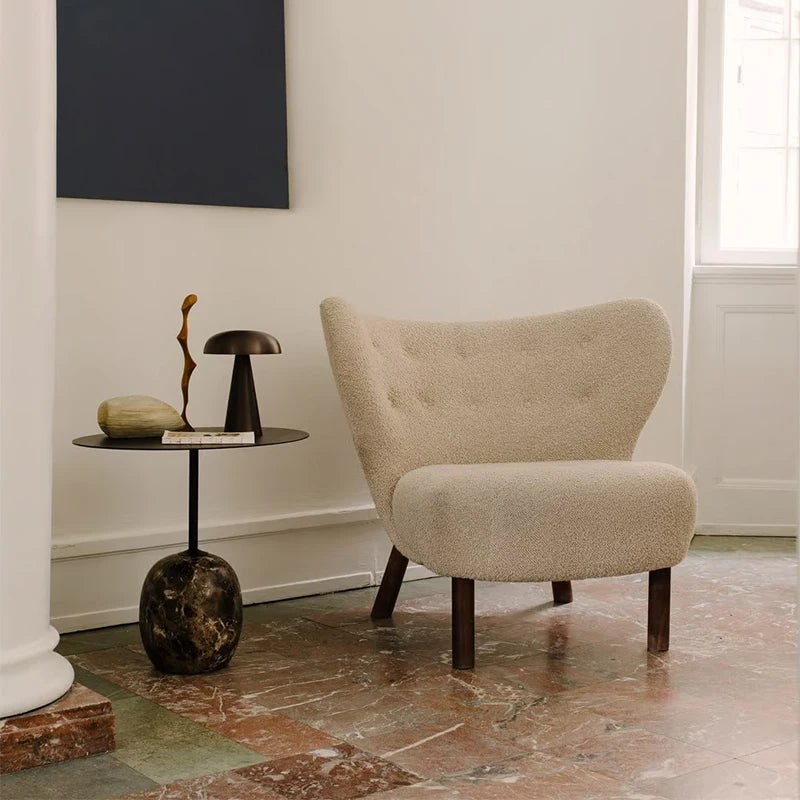 Beige armchair in a room with a small round table and decorative items.