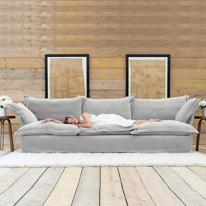 Person lying on a large gray sofa in a room with wooden walls and decor.