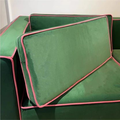 Green cushions with pink piping on a green sofa against a white wall.