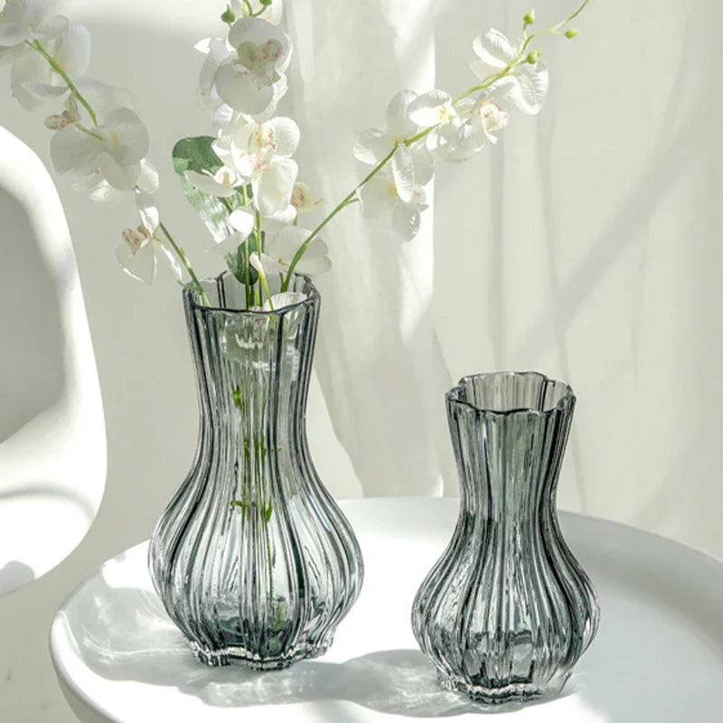 Two ribbed glass vases with white flowers on a white surface.