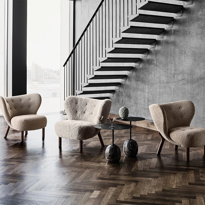 Modern living room with beige armchairs and a coffee table in front of a staircase.