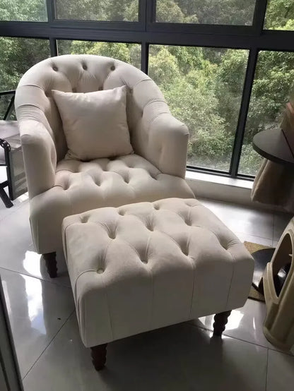 White armchair with ottoman in a room with large windows showing greenery outside