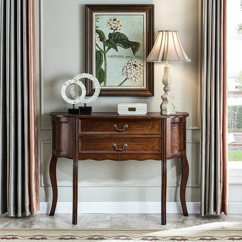 Wooden console table with decorative items in a room with curtains and a lamp.