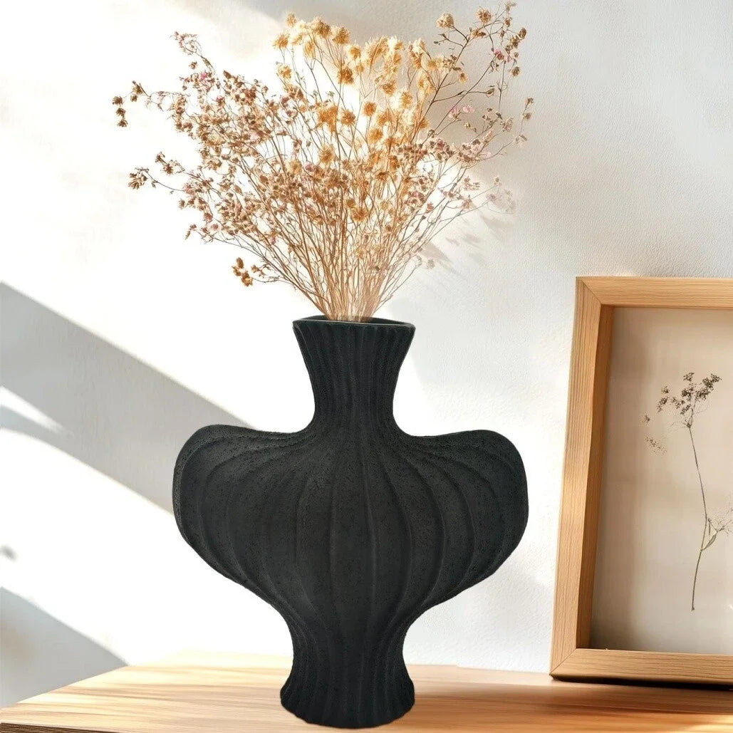 Black textured vase with dried flowers on a wooden surface