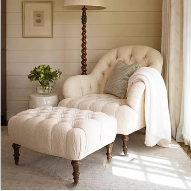 Cozy living room with a white armchair and ottoman, wooden floor lamp, and decorative elements.