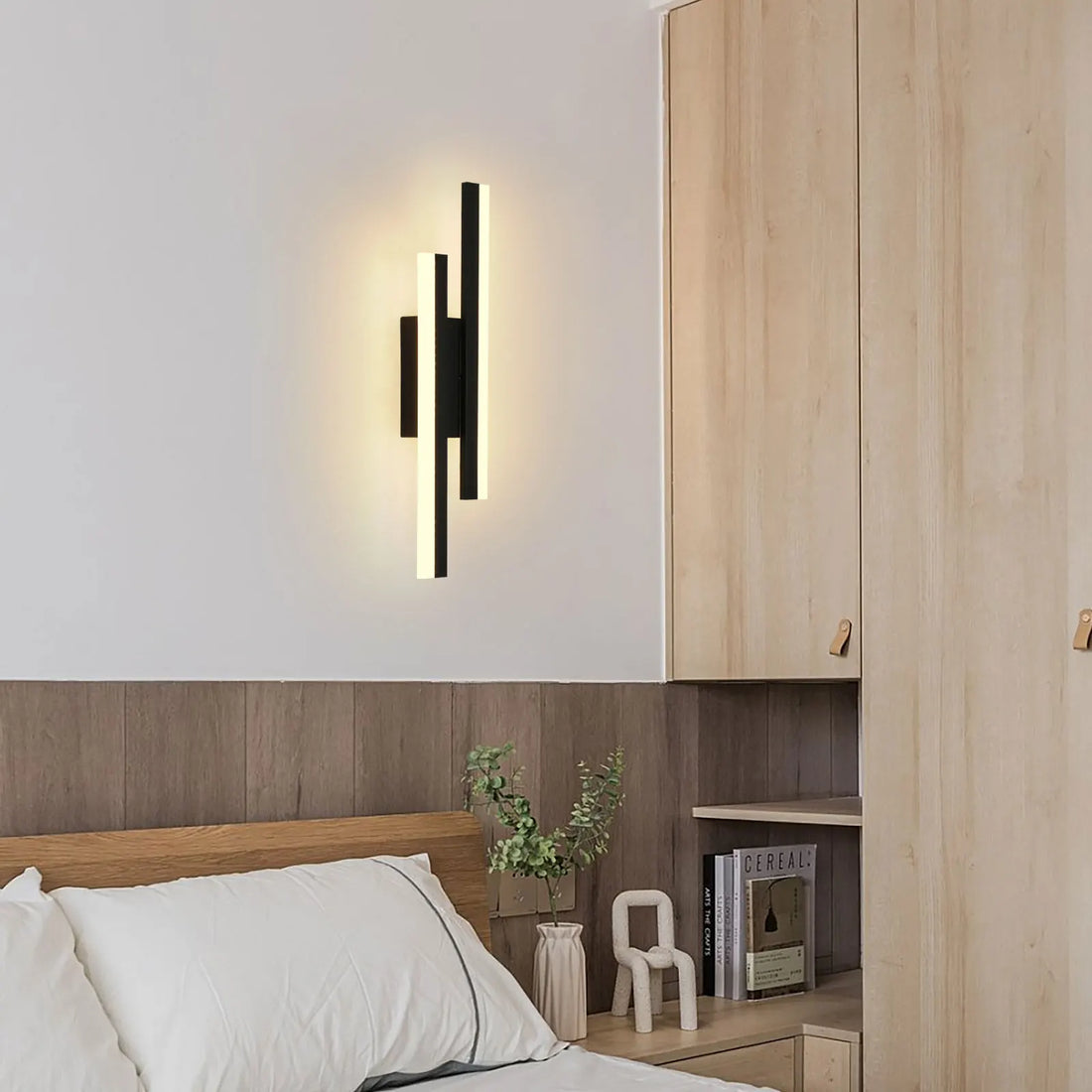 Modern wall sconce in a bedroom setting with wooden headboard and cabinets.