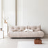 Beige sofa in a minimalistic living room with a white wall and light-colored floor.