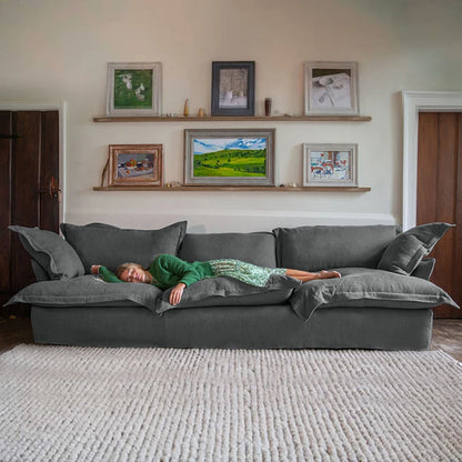 Person lying on a large gray sofa in a room with framed pictures on the wall.