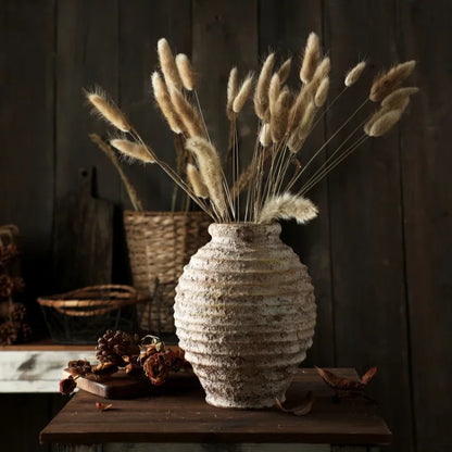 Decorative vase with dried plants on a wooden surface against a dark wooden wall.