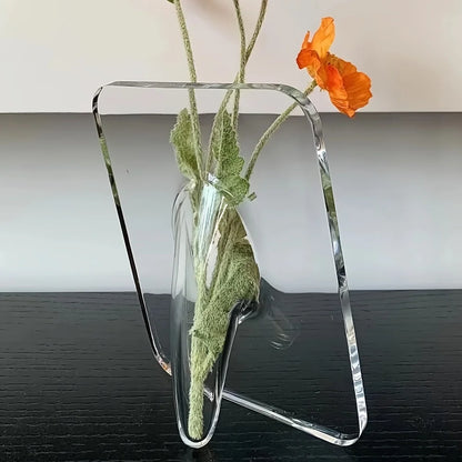 Clear glass vase with a green plant and orange flower on a black surface.