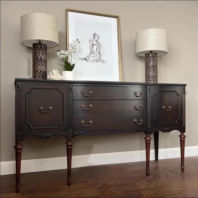 Dark wooden sideboard with lamps and decor against a beige wall