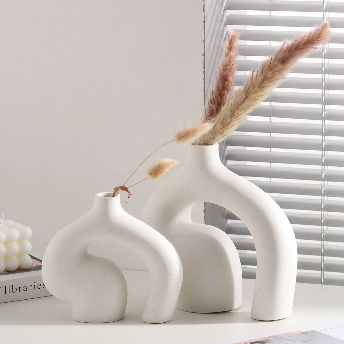 Set of three white ceramic vases with dried pampas grass on a light surface.