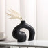 Black vase with dried plants on a white surface with a light background