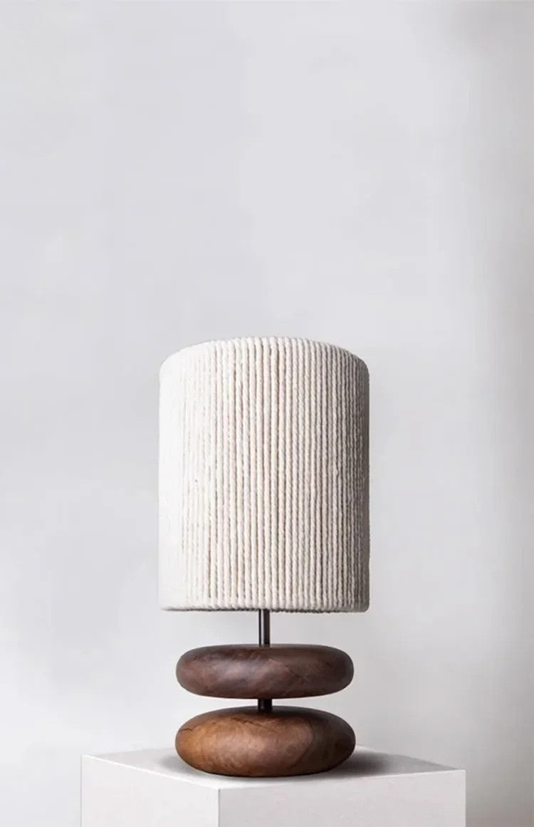 Table lamp with wooden base and textured white shade on a white pedestal against a light gray background