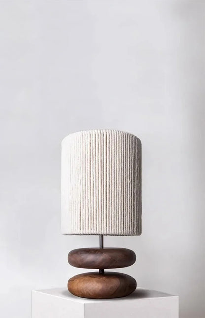 Table lamp with wooden base and textured white shade on a white pedestal against a light gray background