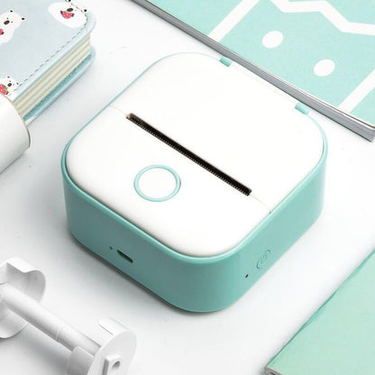 Teal and white electronic device on a light blue surface with stationery items.
